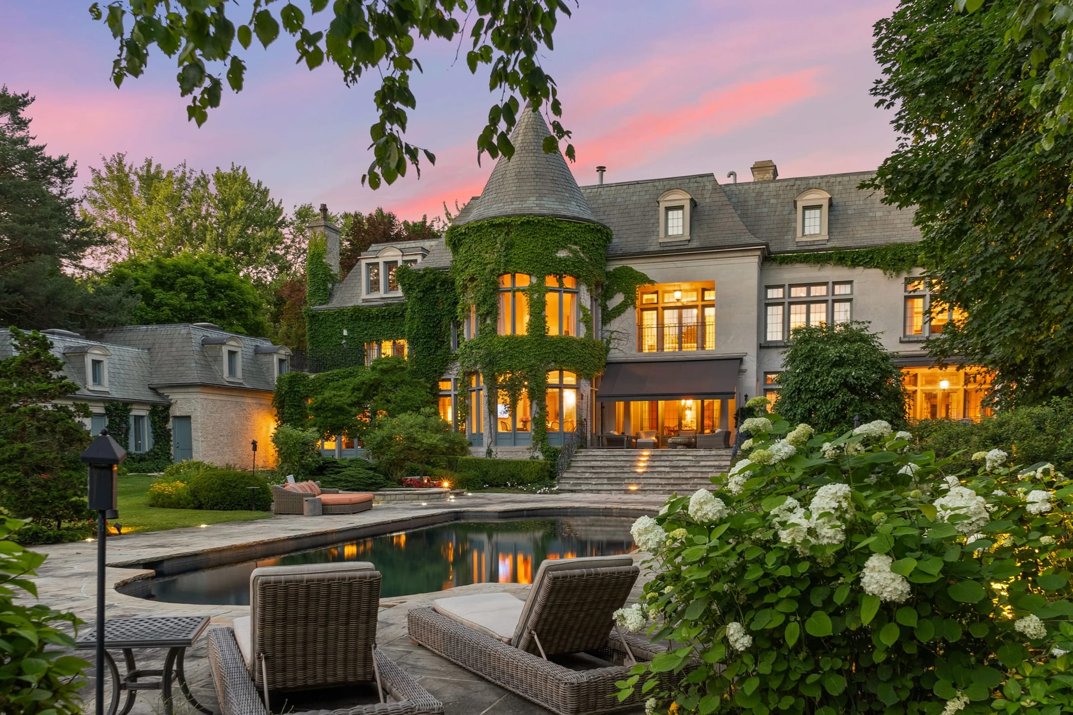 Stone estate with a turret and pool terrace at dusk, represented by Cohen Homes and Estates